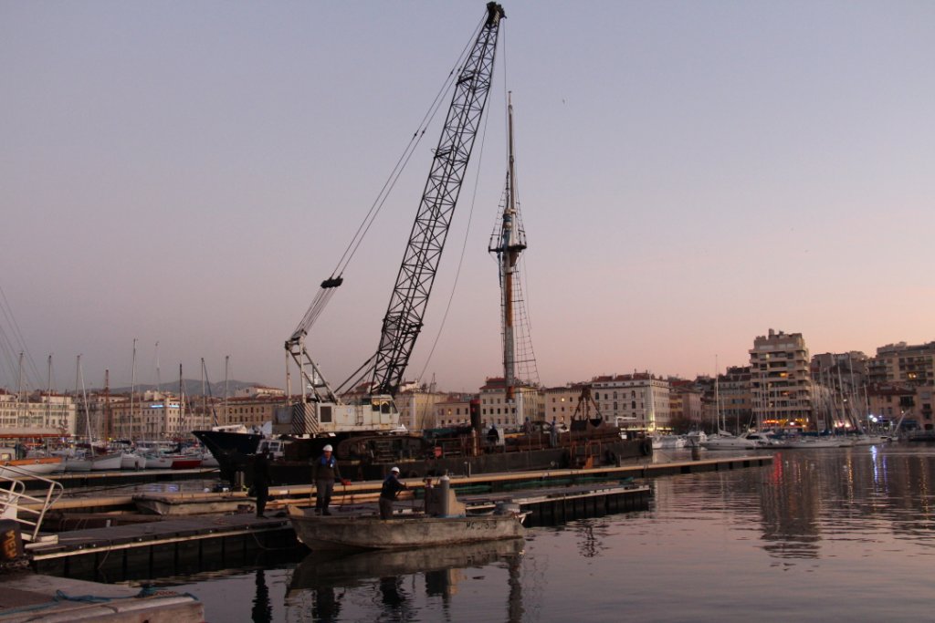 Un ponton-grue équipé d’un engin de levage amarré à proximité du Marseillois soulève un des mâts (Photo Philippe Maillé)